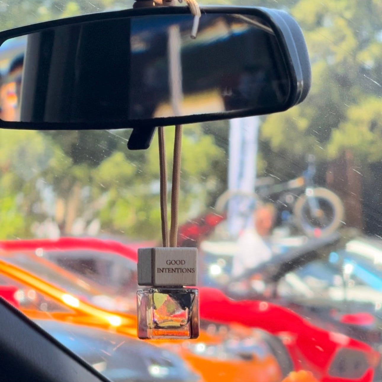 Car air freshener hanging from a car's rearview mirror with a blurred outdoor background.